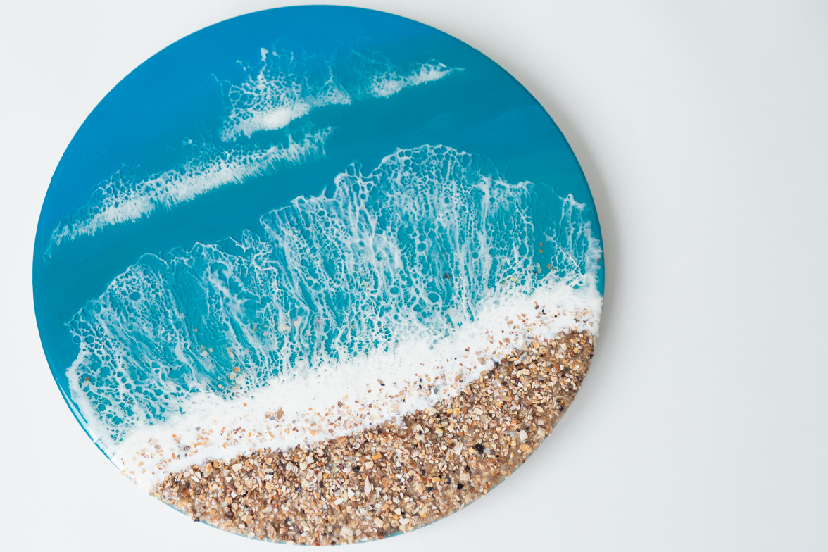 Round resin art painting with blue ocean waves and beach on white background. Epoxy resin art